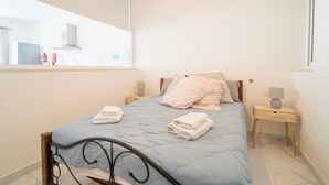 A bedroom with a bed, two bedside tables, a window, and a mirror. - Cozy Apartment with Balcony in Xlendi Bay, Gozo (Munxar)