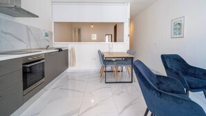A modern kitchen with a built-in oven, a dining area with a table and chairs, and a large window. - Cozy Apartment with Balcony in Xlendi Bay, Gozo (Munxar)