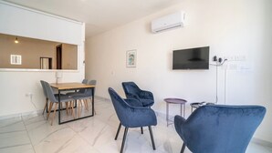 A modern living room with a dining area, a flat-screen TV mounted on the wall, and a built-in air conditioning unit. - Cozy Apartment with Balcony in Xlendi Bay, Gozo (Munxar)