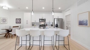 A modern kitchen with white cabinetry, stainless steel appliances, and a central island with bar stools.