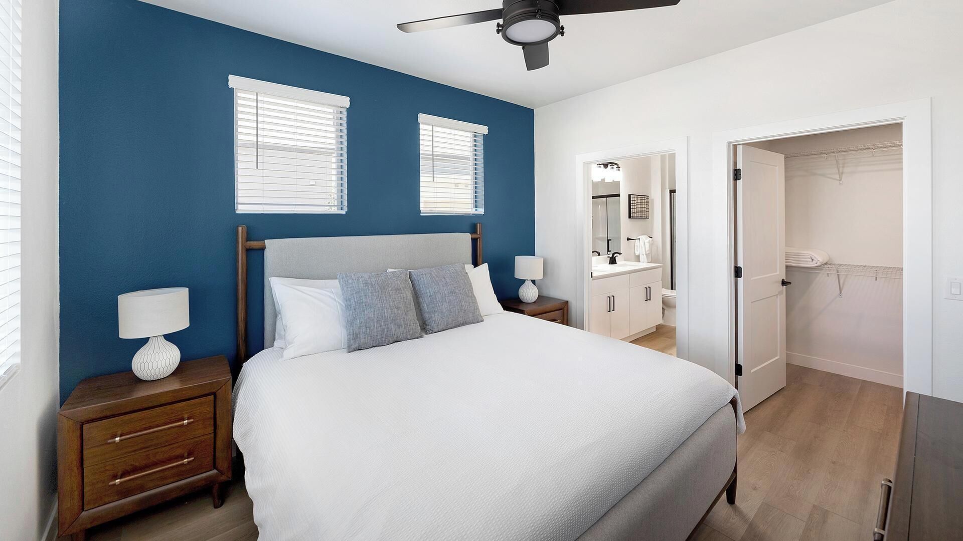 A bedroom with a bed, two bedside tables, a ceiling fan, and a walk-in closet.