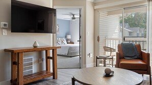 A modern living room with a flat-screen TV, a wooden console table, a round coffee table, a brown leather sofa, and a balcony with a view of houses. - Landing | Chic 2BD, Gym, Clubhouse (Eureka)