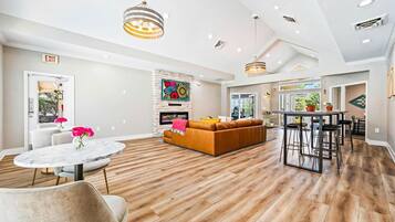 A spacious living area with a wooden floor, a round marble table, a brown sofa, and a modern pendant light.