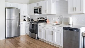 A modern kitchen with white cabinets, stainless steel appliances, and a wooden floor. - Landing | Spectacular 1BD, Gym, Pool (Bellview)