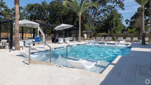 Una piscina con lettini e ombrelloni, circondata da palme e un patio in mattoni.