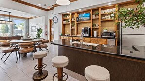 Cocina moderna con una isla central, taburetes de bar, estantes de madera con adornos y un amplio ventanal que proporciona luz natural.