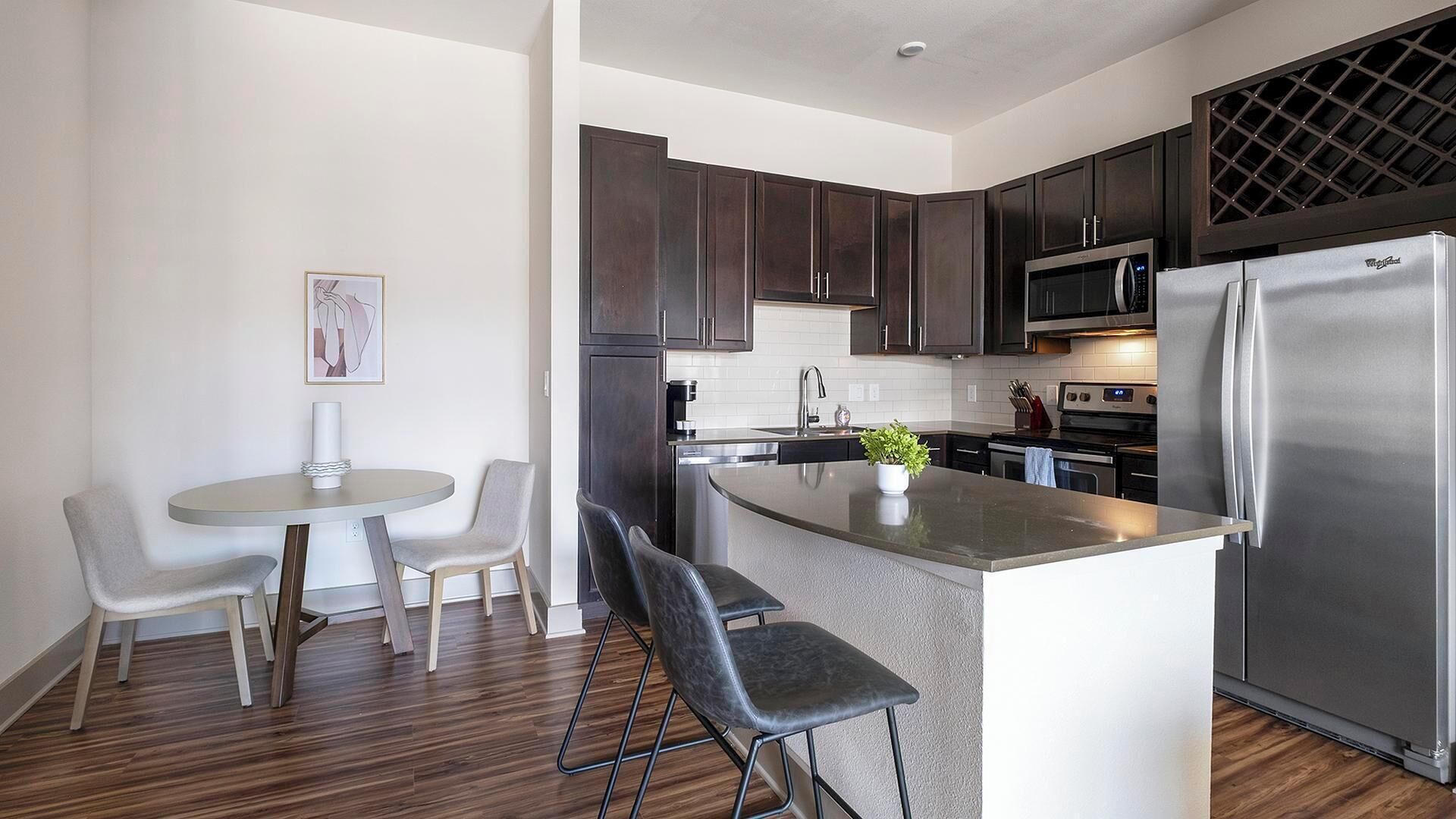 Una cocina moderna con armarios de madera oscura, electrodomésticos de acero inoxidable y una isla central con taburetes de bar.