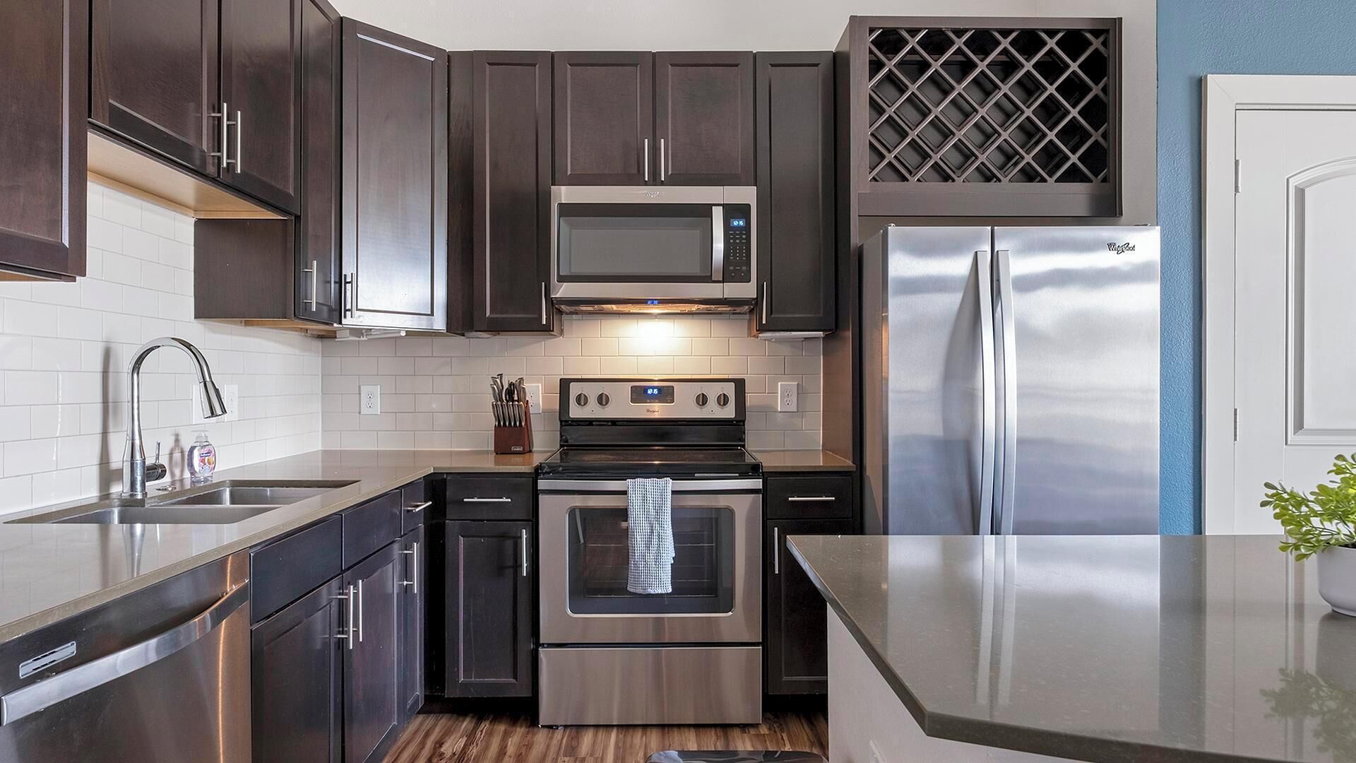 A modern kitchen with dark cabinetry, stainless steel appliances, and a white tiled backsplash.