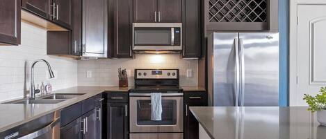 A modern kitchen with dark cabinetry, stainless steel appliances, and a white tiled backsplash.