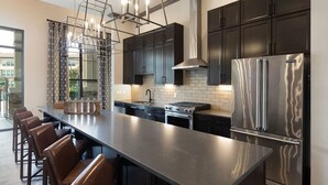 Una cocina moderna con armarios oscuros, electrodomésticos de acero inoxidable y una isla grande con taburetes de bar.