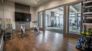 Een ruime fitnessruimte met spinningfietsen, een televisie en gewichthefapparatuur.