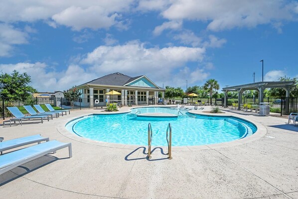A swimming pool with lounge chairs and a covered area, surrounded by a building with large windows.