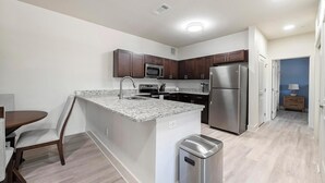 A modern kitchen with granite countertops, stainless steel appliances, and wooden cabinets. - Landing | Chic 2BD, Pool, Gym (Lockhart)