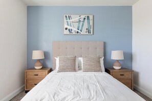 Quarto com cama, duas mesas de cabeceira, duas luminárias e uma obra de arte na parede.