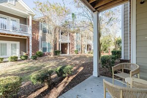 A residential building with a covered porch, a brick facade, and a landscaped yard with shrubs and a gravel path.