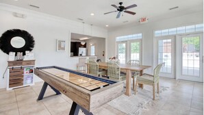 Una habitación amplia con mesa de billar, un comedor con sillas de mimbre y ventanas grandes.