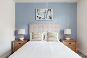 A bedroom with a large bed, two bedside tables, and a wall-mounted abstract painting.