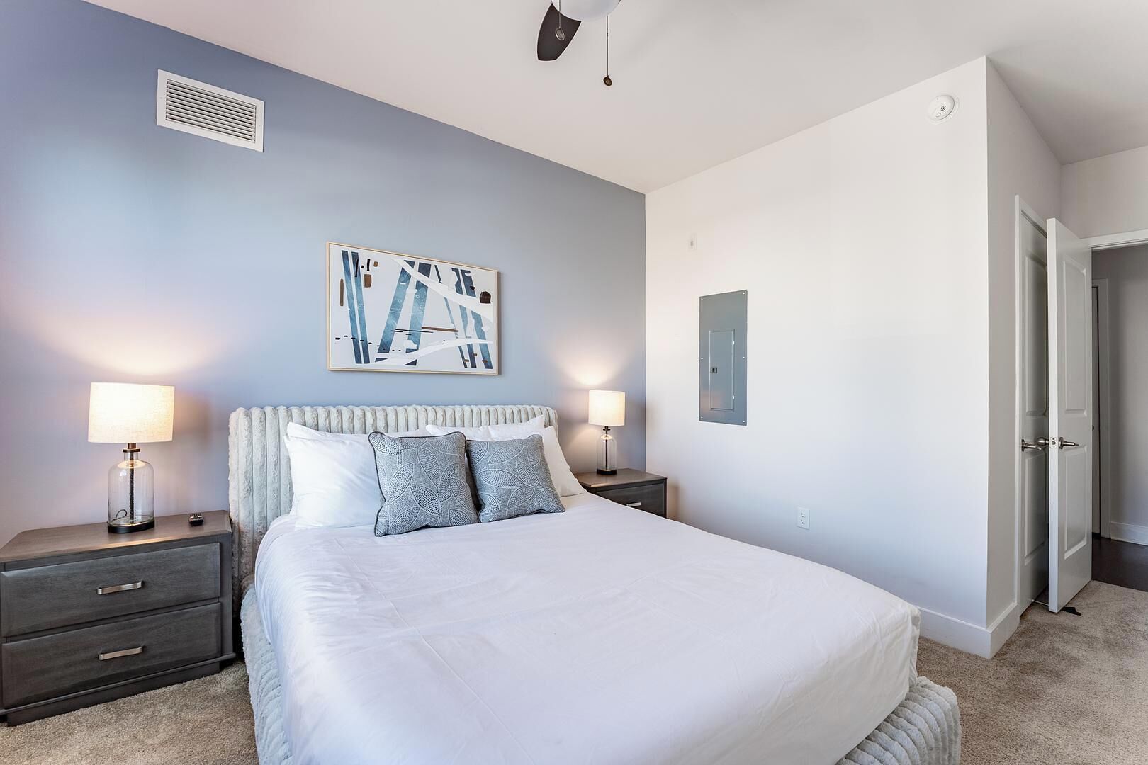 Une chambre moderne avec un grand lit, deux tables de chevet avec des lampes, un radiateur, un interrupteur fixé au mur et une porte donnant sur une autre pièce.