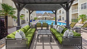 A covered outdoor seating area with a pool, green cushioned sofas, and lounge chairs. - Landing | Stunning 2BD, Gym (Monroe)