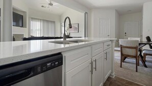 A modern kitchen with a dishwasher, white cabinetry, and a large island with a sink. - Landing | Stunning 2BD, Gym (Monroe)