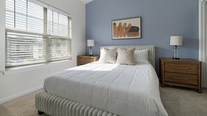 A bedroom with a bed, two nightstands, a lamp, a wall art piece, and a window with blinds. - Landing | Stunning 2BD, Gym (Monroe)