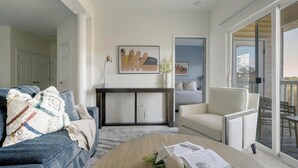 A modern living room with a sofa, a coffee table, and a chair. There is a painting on the wall and a door leading to another room. - Landing | Spectacular 2BD, Gym (Monroe)