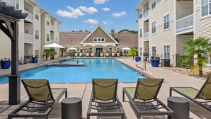 A swimming pool with lounge chairs, a covered seating area, and a building with a gabled roof in the background. - Landing | Stylish 2BD, Gym (Monroe)