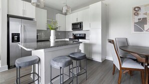 A modern kitchen with a central island, bar stools, a dining table with chairs, and a microwave. - Landing | Stunning 2BD, Gym (Saint Johns)