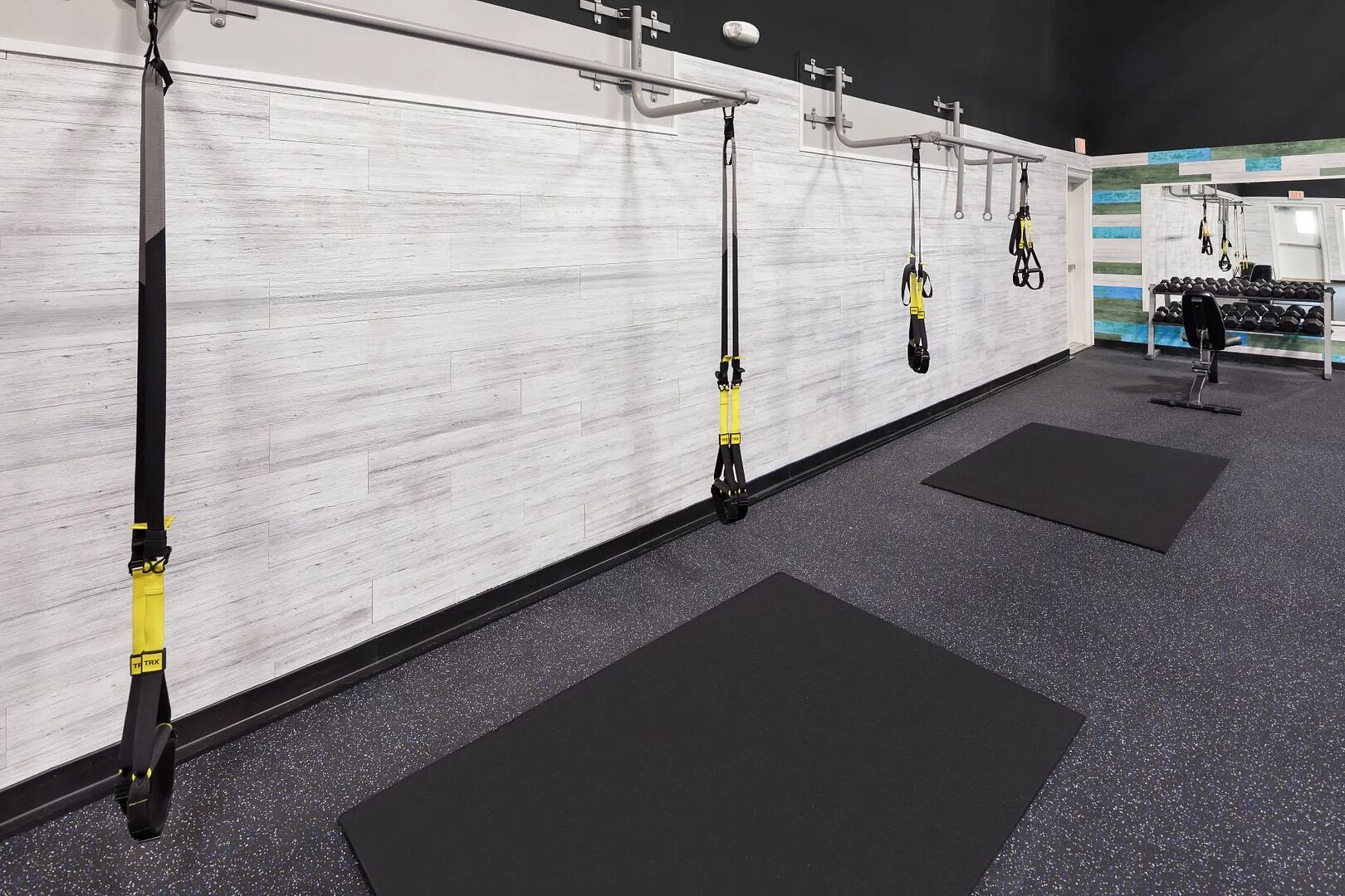 A gym with TRX suspension straps, weight plates, and black mats on the floor.