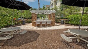An outdoor patio with a barbecue area, seating, and umbrellas. - Landing | Modern 1BD, Yoga Studio (Jacksonville)