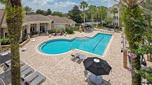 A swimming pool with lounge chairs and umbrellas, surrounded by palm trees and a brick patio. - Landing | Modern 1BD, Yoga Studio (Jacksonville)