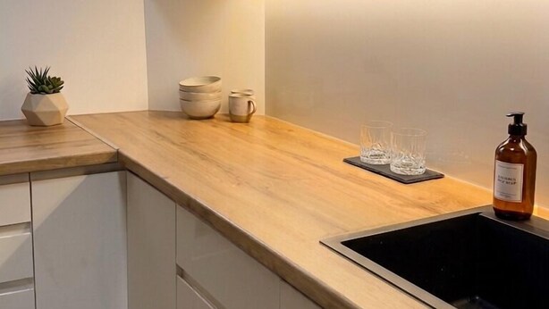 A modern kitchen with wooden cabinets, a black sink, and a window with a view of a house. - Oficerski apartment (Bitola)
