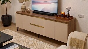 A living room with a flat-screen TV on a wooden cabinet, a potted plant, a candle, and a book on a coffee table. - Oficerski apartment (Bitola)