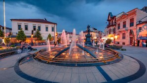 A circular fountain with water jets in a public square surrounded by historic buildings. - Oficerski apartment (Bitola)