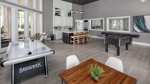 Una cucina moderna con mobili bianchi, un'area pranzo con tavolo e sedie in legno, un tavolo da calcio e un'ampia finestra che offre luce naturale.