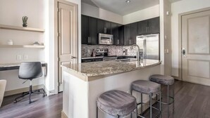 Une cuisine moderne avec des meubles de couleur sombre, des appareils en acier inoxydable, un comptoir en granit et un coin bar avec des tabourets.