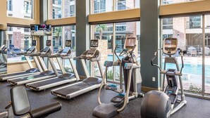 Une salle de sport équipée de tapis de course, de vélos elliptiques et offrant une vue sur la piscine.