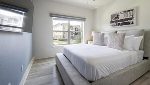 Quarto com uma cama grande, janela com persianas, obra de arte na parede e vista exterior visível.