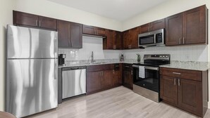 A modern kitchen with dark wood cabinets, stainless steel appliances, and a granite countertop. - Landing | Incredible 1BD, Gym, Pool (Lockhart)