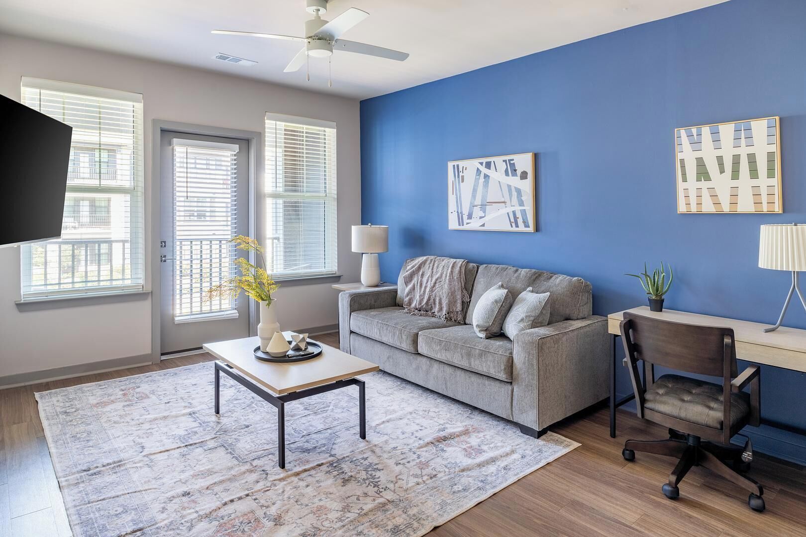 Ein Wohnzimmer mit grauem Sofa, Couchtisch, Schreibtisch mit Stuhl und blauer Akzentwand.