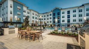 A hotel courtyard with a pool, outdoor seating, and grilling areas. - Landing | Beautiful 1BD, Game Room, Pool (Freeport)