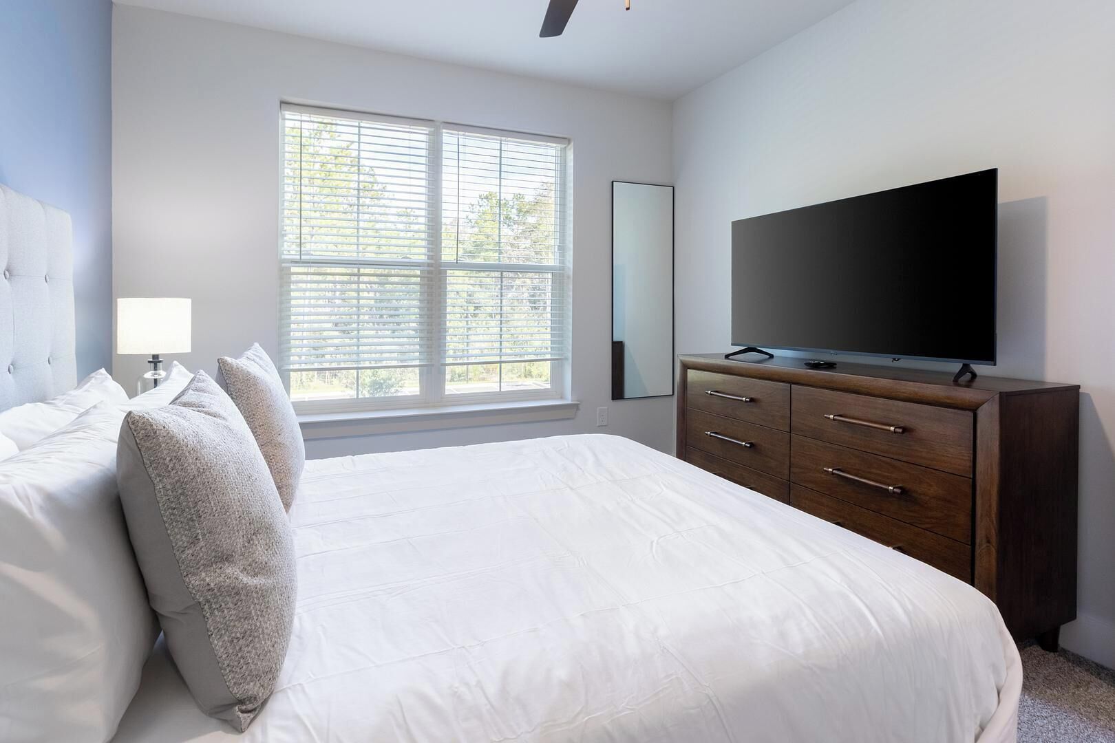 Un dormitorio con una cama grande, un aparador, un televisor de pantalla plana y una ventana con persianas.