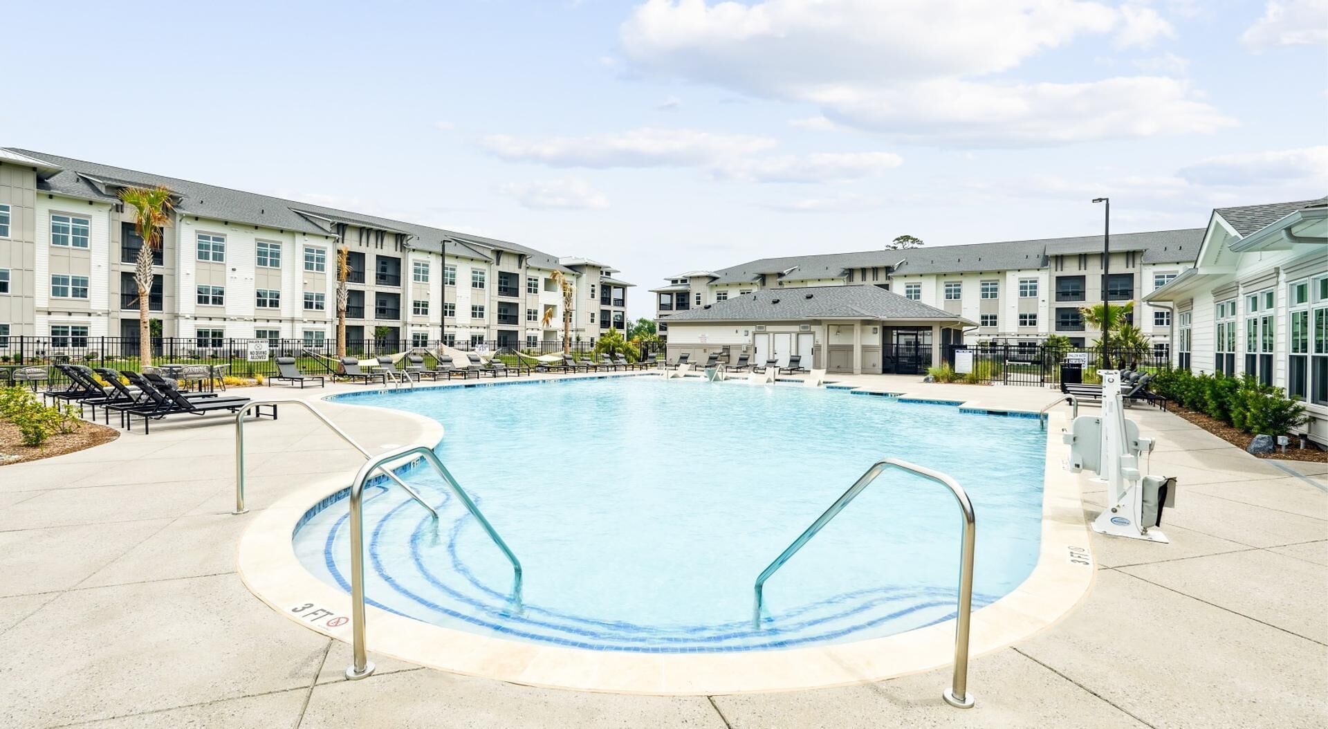 A swimming pool surrounded by a building with multiple floors, outdoor seating, and a clear sky.
