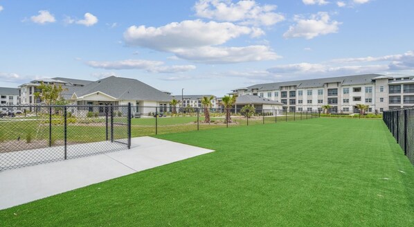A well-maintained grassy area with a fence, surrounded by modern buildings with multiple floors and balconies.