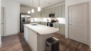 Une cuisine moderne avec des meubles blancs, des appareils en acier inoxydable et un îlot central.