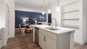 Une cuisine moderne dotée d’un îlot central, d’un coin repas avec des chaises et d’un mur d’accent bleu.