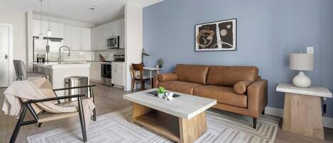 Una sala de estar moderna con un sofá marrón, una mesa de centro y un comedor con una cocina al fondo.