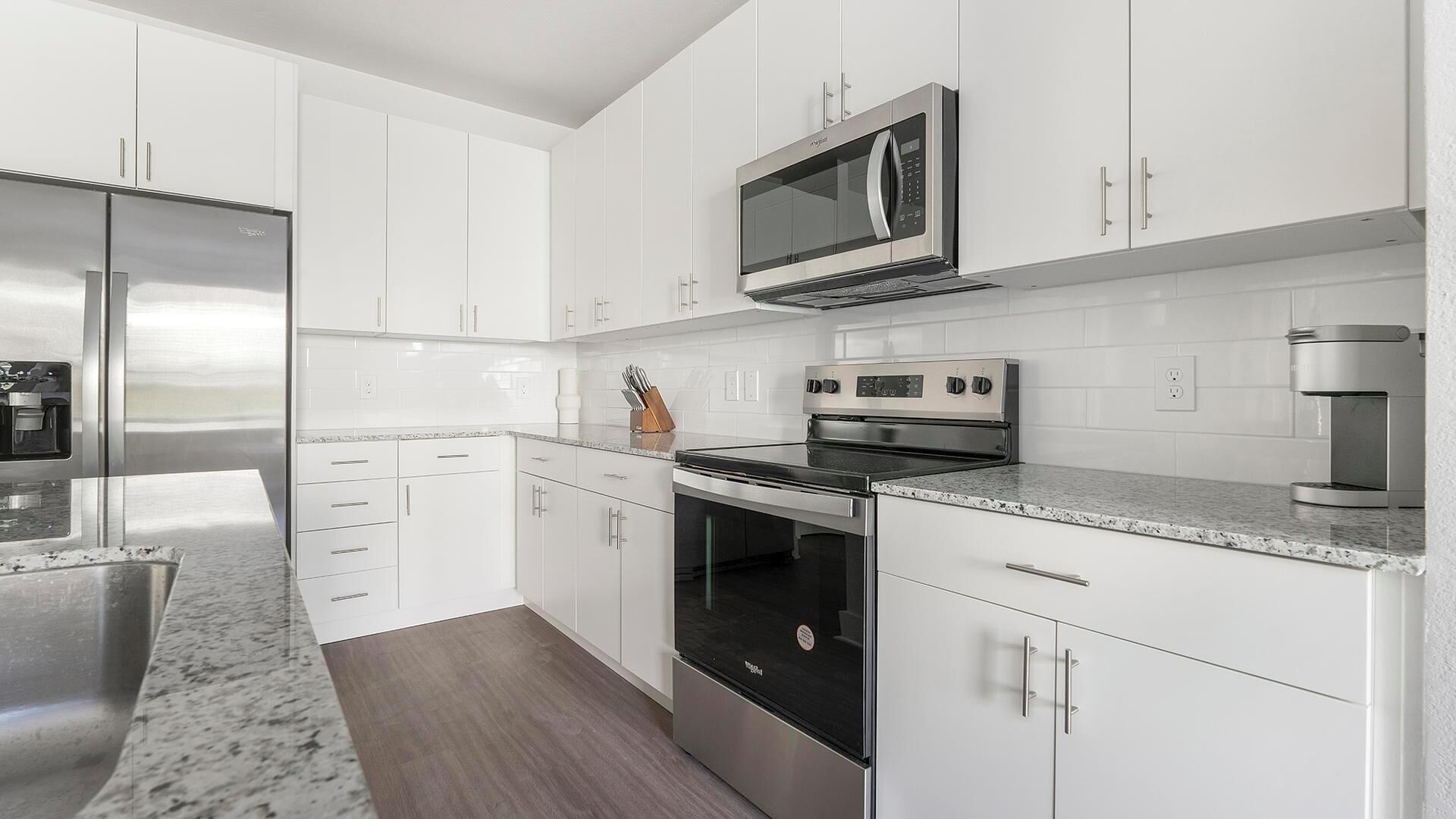 A modern kitchen with white cabinetry, stainless steel appliances, and a granite countertop.