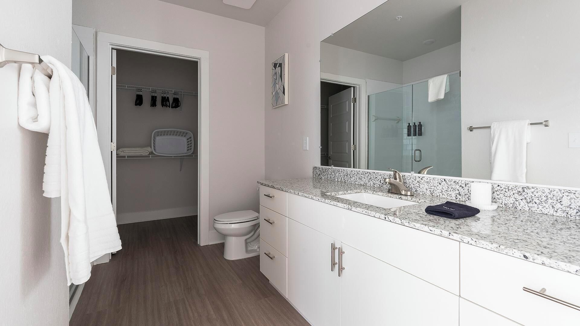 Moderni kylpyhuone, jossa on valkoinen allaskaappi, suuri peili ja suihkutila.