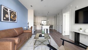 Een moderne woonkamer met een bruine leren bank, een glazen salontafel en een flatscreen televisie die aan de muur is bevestigd.